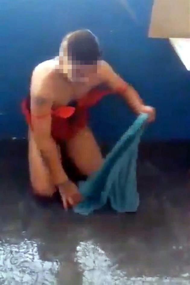 Uno de los reos porta un babydoll, mientras seca el agua del piso con una toalla.