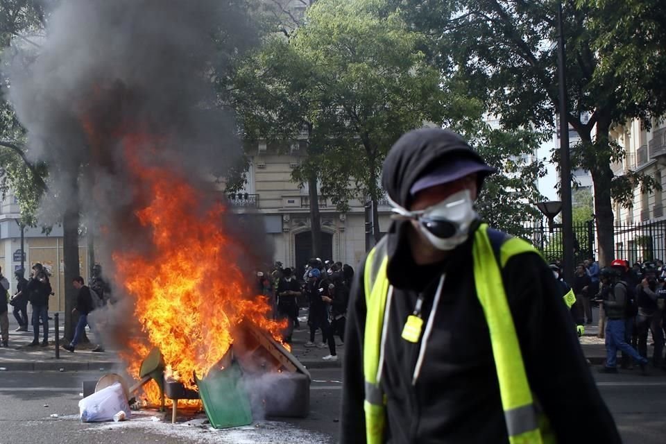 Un manifestante pasa junto a un bote de basura incendiándose, en París.