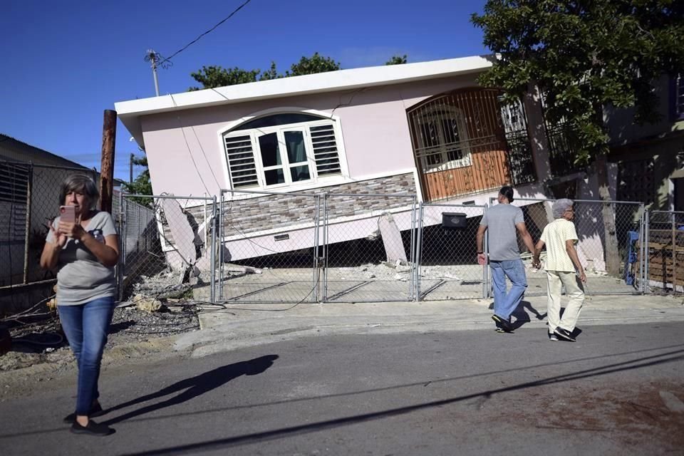 Residentes caminan frente a una casa caída por el sismo en Puerto Rico.