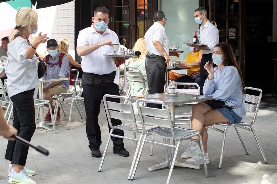 Un camarero atiende a una clienta en la terraza del Café Zurich una de las 5 mil 500 terrazas de restaurantes y bares de Barcelona que reabren este lunes.