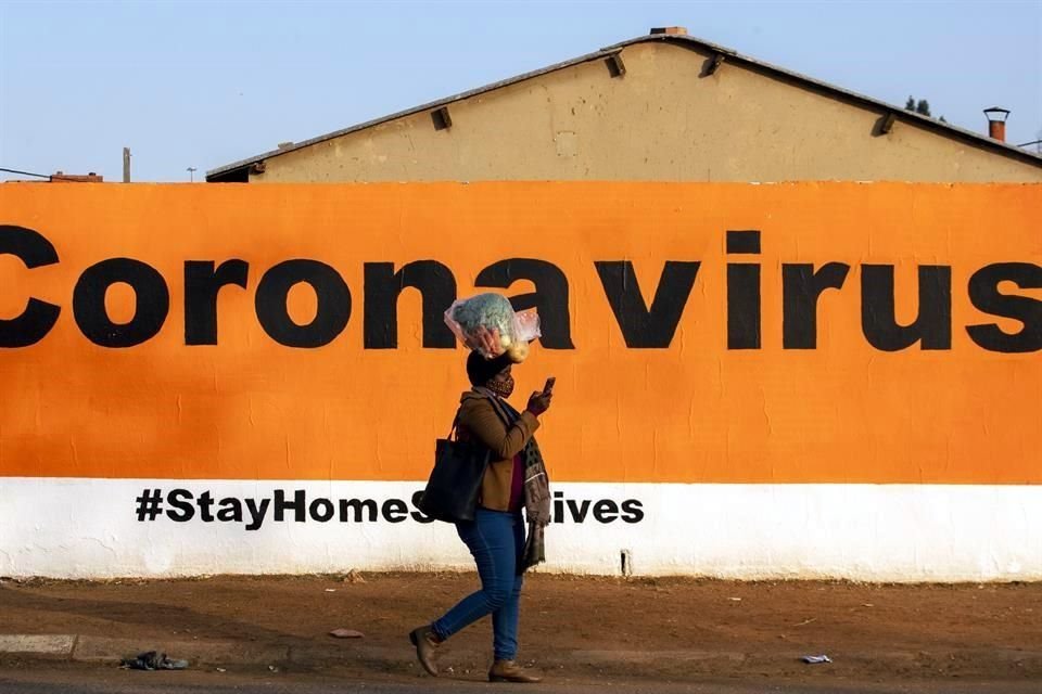 Una mujer camina cargando una bolsa de verduras sobre la cabeza, junto a un mural que pide quedarse en casa, en Soweto, Sudáfrica.