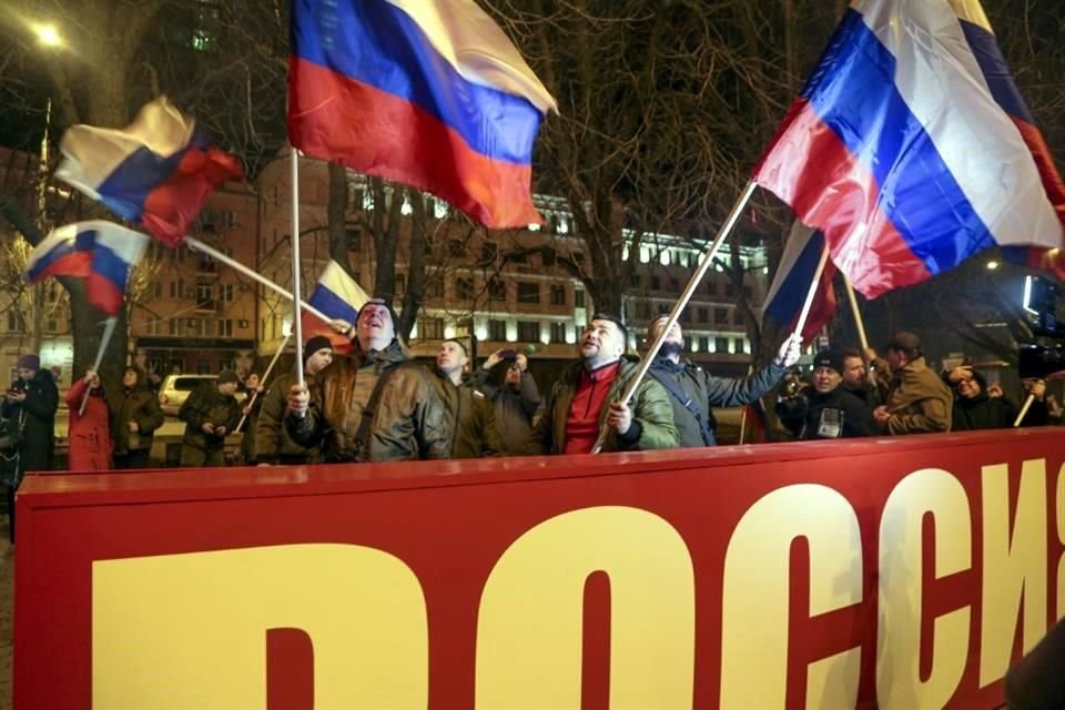 Personas ondean la bandera rusa junto a un mensaje que dice 'Rusia, en el centro de Donetsk, tras el anuncio de Putin sobre el reconocimiento a las regiones separatistas