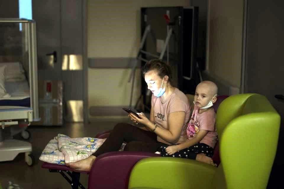 Una madre observa su teléfono junto a su hija, mientras se refugian en el sótano del hospital.