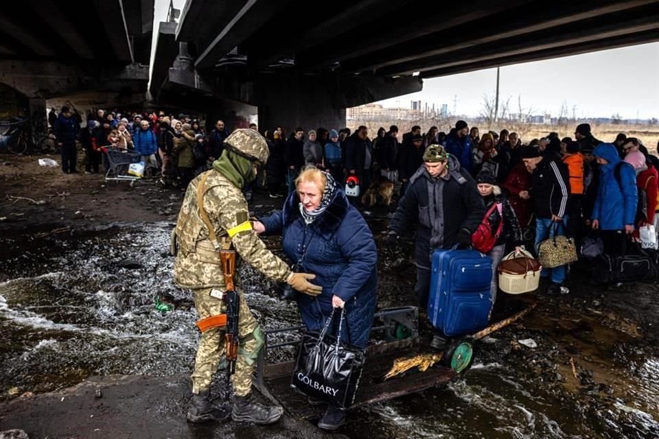 Un soldado ucraniano ayuda a civiles a escapar de Irpin, debajo de un puente bombardeado por las fuerzas rusas.