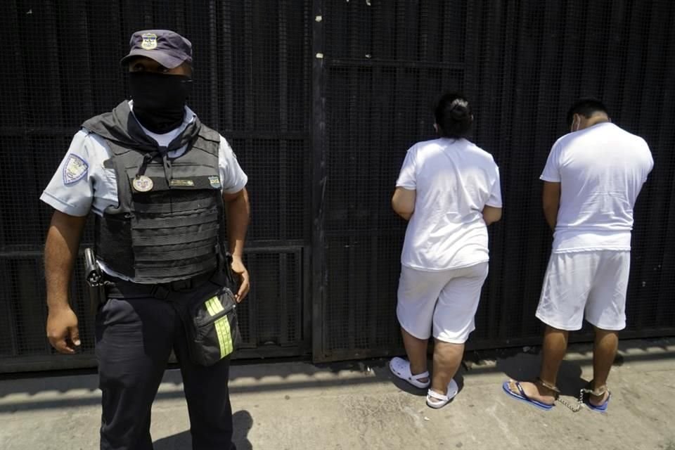 Un agente de la Policía Nacional Civil salvadoreña vigila a dos personas detenidas durante un operativo de seguridad, en el departamento de San Salvador.
