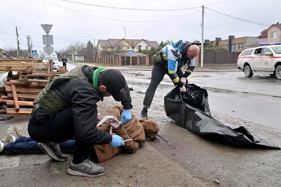 Un trabajador comunitario libera las manos de un cadáver hallado en Bucha, afuera de Kiev, mientras su colega prepara una bolsa para transportarlo.