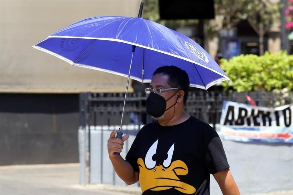 Persona camina por el Centro de Guadalajara y trata de protegerse de la radiación solar del mediodía usando paraguas.