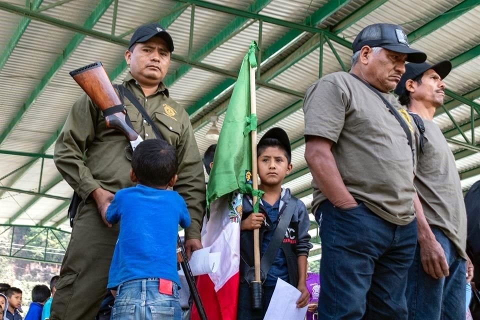 Dos niños, en medio de una bandera y policías armados, esperan la orden de marchar en Ayahualtempa, comunidad que Los Ardillos, grupo criminal, asedia con asesinatos y extorsiones.