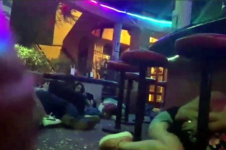 Parejas abrazadas y tiradas en el piso, bajo sillas y mesas se observan en videos de balacera.