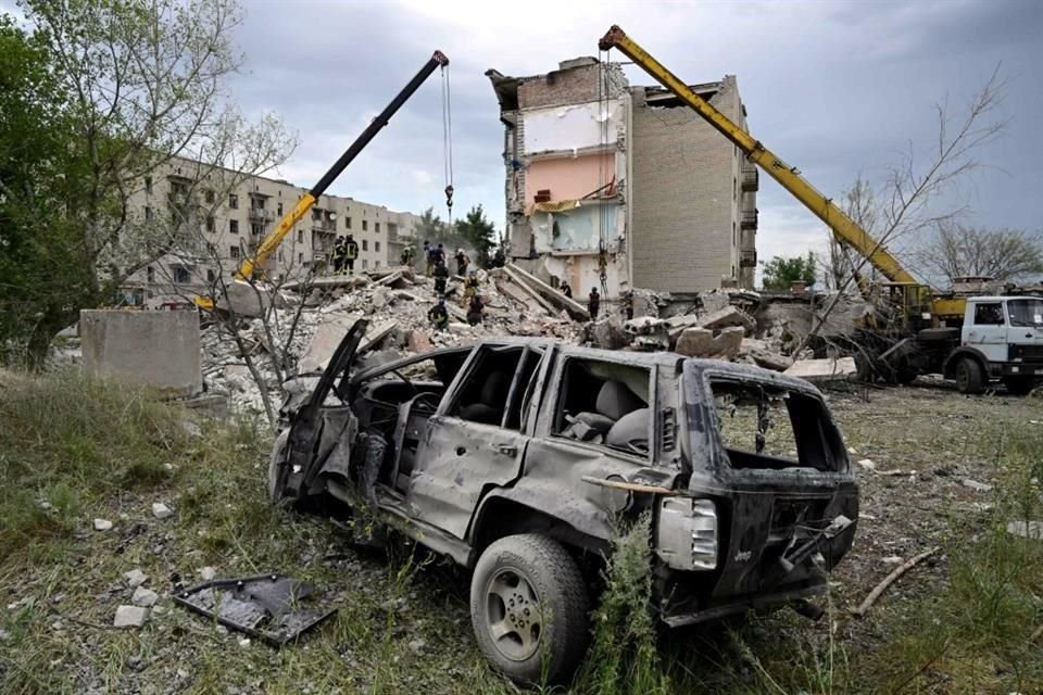 Un auto luce destrozado, mientras al fondo, los rescatistas buscan sobrevivientes.