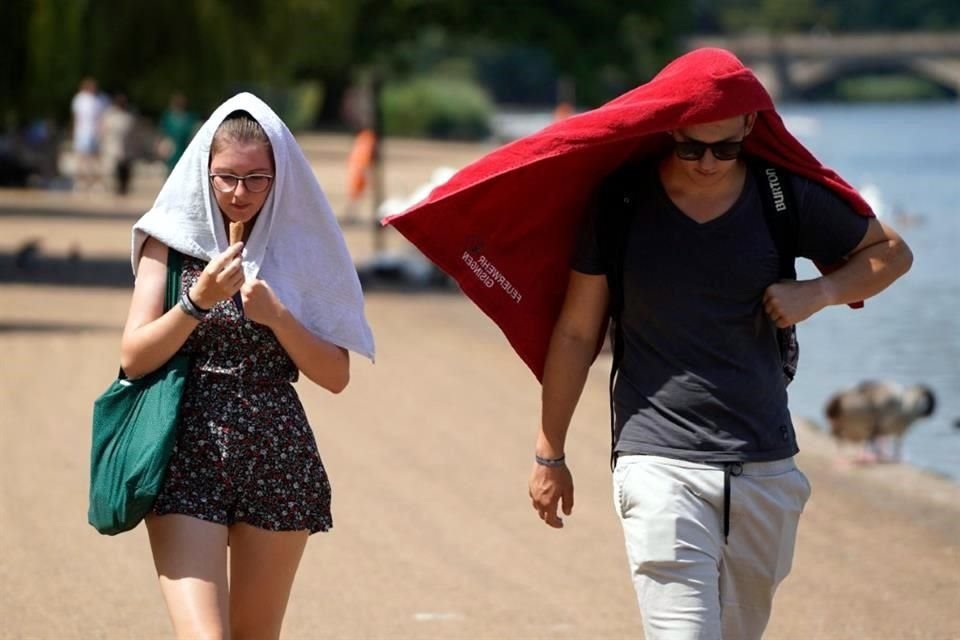 Personas se cubren la cabeza de los rayos del sol en Hyde Park, Londres.