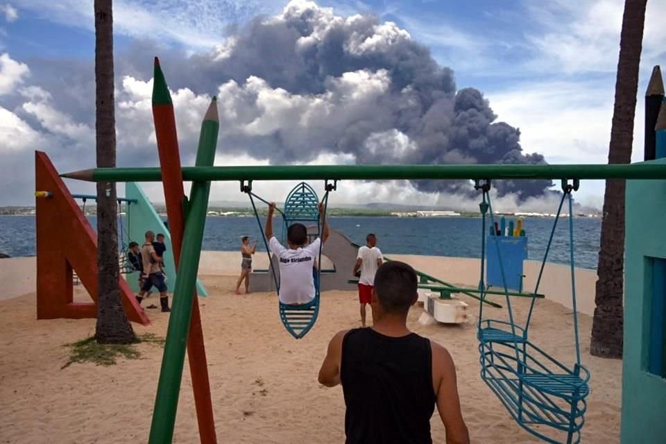 Niños juegan en un parque en Matanzas, Cuba. Al fondo se aprecia el humo del incendio en los depósitos de combustible.