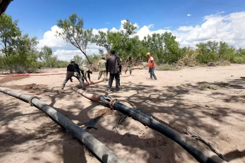 Trabajadores y militares que colaboran en el rescate de los 10 mineros atrapados en la mina 'El Pinabete' acomdan una manguera para el desfoga de agua.