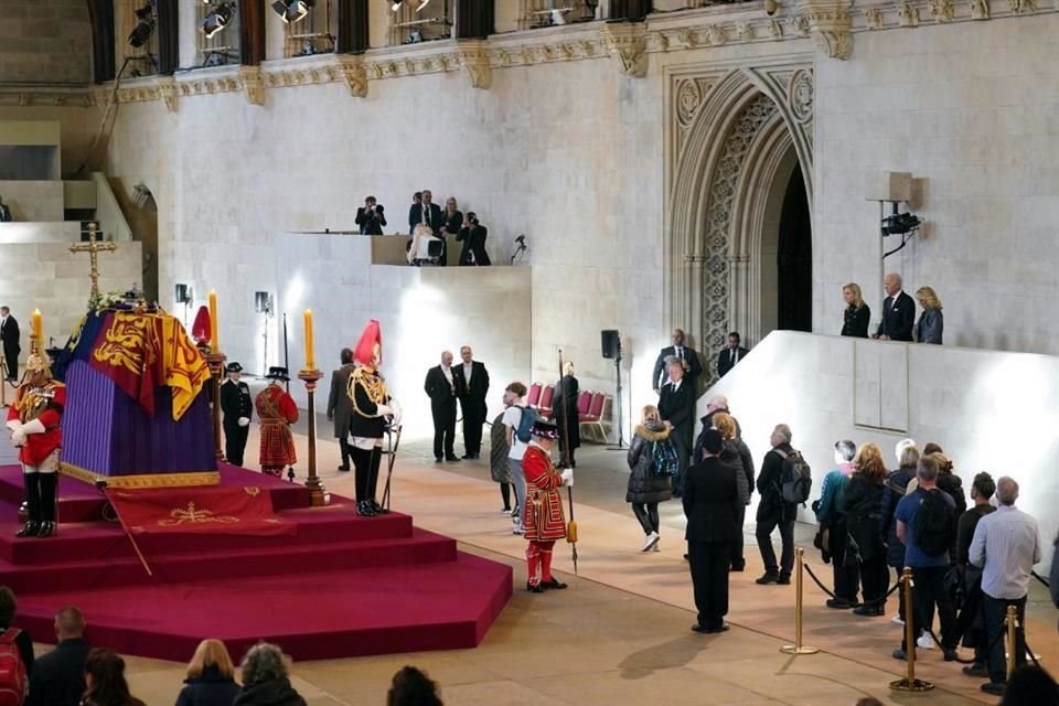 A la derecha, el Presidente Joe Biden y su esposa se asoman por un balcón para presentar sus respetos a la Reina Isabel II.