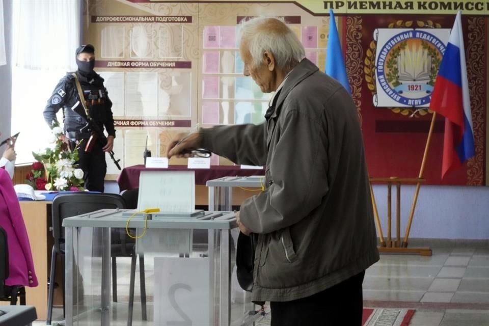 Un hombre deposita su boleta en una consulta sobre la anexión a Rusia, en Lugansk, mientras un militar vigila.