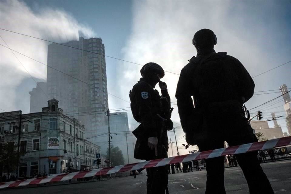 Oficiales de Policía hacen guardia con el humo de ataques rusos de fondo.