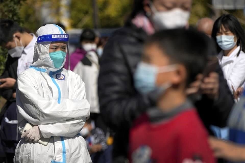 Un trabajador con traje protector observa mientras residentes se toman muestras para pruebas de Covid-19, en Beijing.