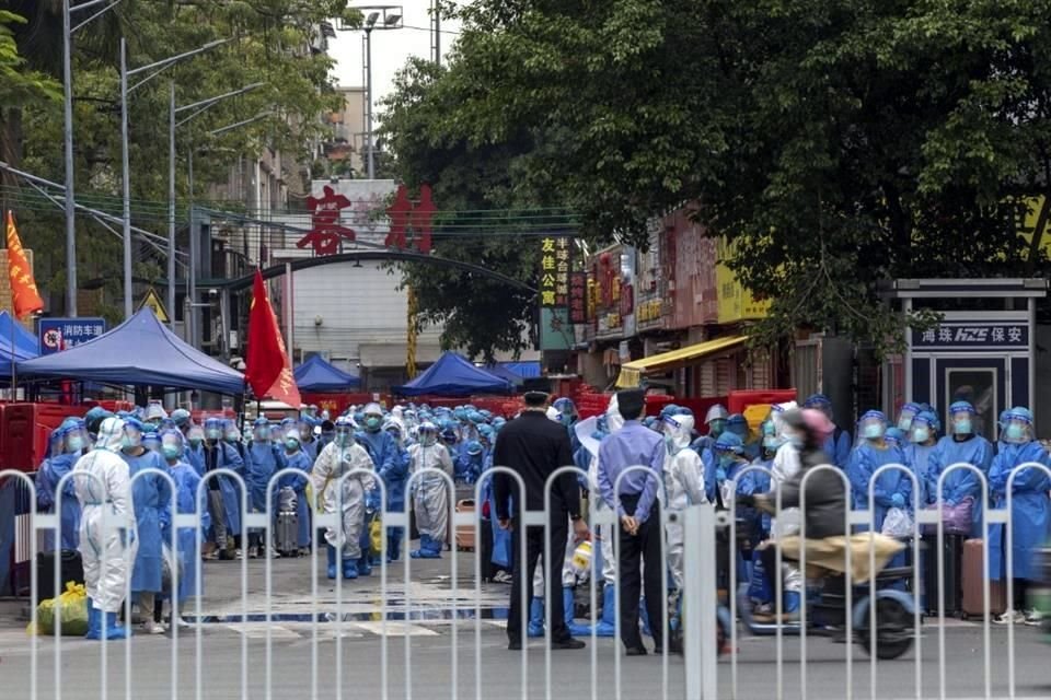 Agentes que usan trajes protectores blancos se preparan para transferir a los residentes (vestidos de azul) a una villa, luego de un alto riesgo de infección por Covid-19 en Guangzhou, en China.