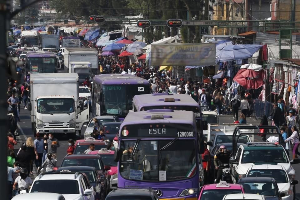 Los compradores caminan sobre el arroyo vehicular entre motocicletas y automóviles.