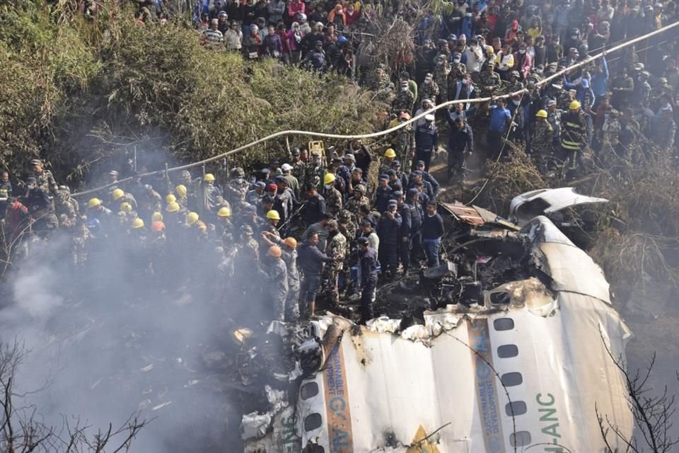 Trabajadores de rescate y civiles nepaleses se reúnen alrededor de los restos de un avión de pasajeros que se estrelló en Pokhara.