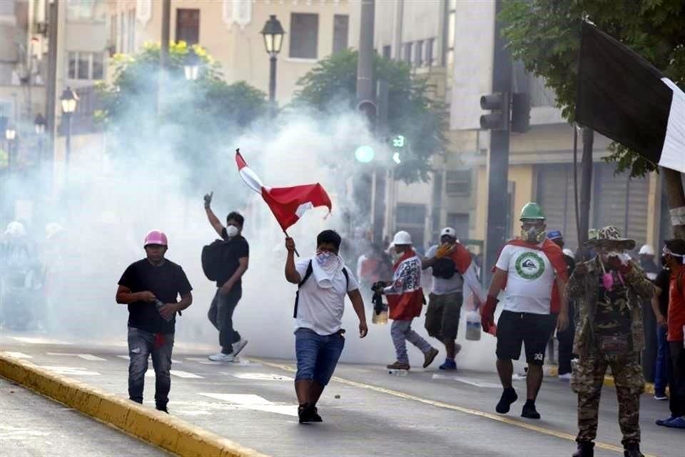 Manifestantes antigubernamentales se cubren del gas lacrimógeno lanzado por la policía para replegar a los movilizados.