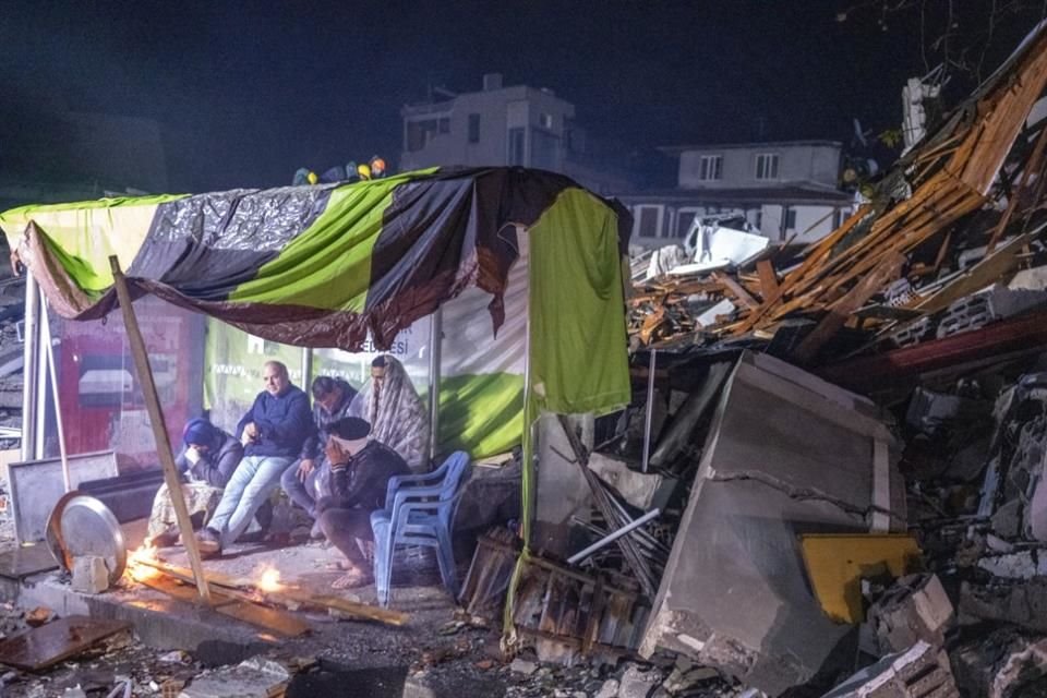 Personas descansan junto a una fogata, a un lado de los escombros de un edificio en Turquía.