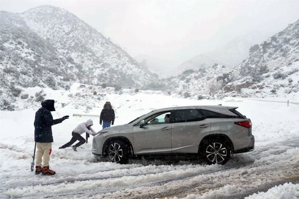 Una persona ayuda a sacar un vehículo que quedó atascado en la nieve en una carretera en las montañas de San Gabriel en el Bosque Nacional Ángeles, California.