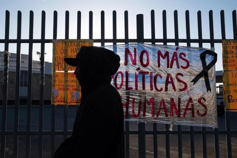 Un migrante pasa junto a un letrero que dice 'No más políticas inhumanas' después de pasar la noche afuera del centro de detención donde 38 migrantes murieron durante un incendio en Ciudad Juárez.