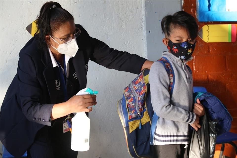 Aplican desinfectante a mochilas de niños.
