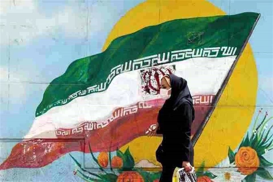 Una mujer pasa frente a una bandera iraní pintada en una pared en una calle de Teherán.