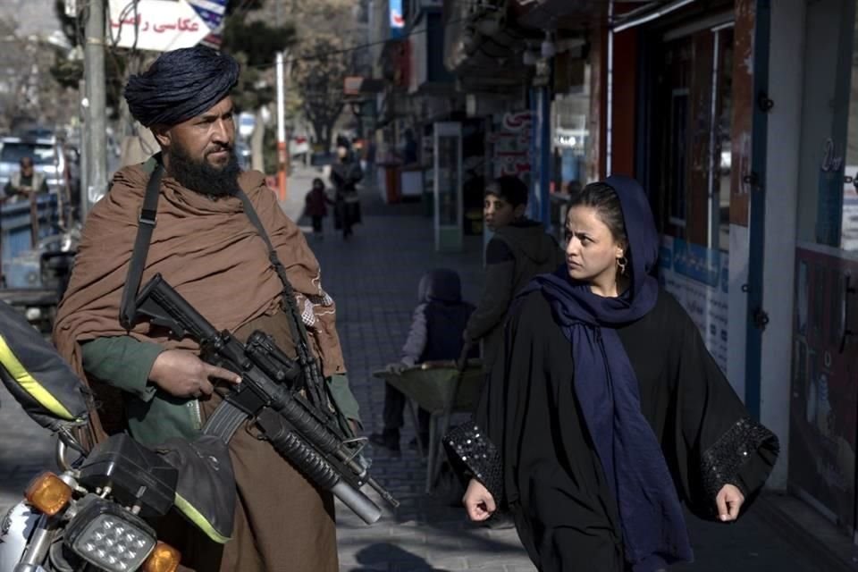 Un combatiente talibán monta guardia mientras una mujer pasa caminando en Kabul, Afganistán.