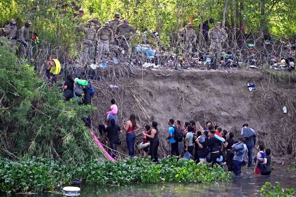 Migrantes que cruzaron el río Bravo son detenidos por miembros de la Guardia Nacional de EU que colocan una cerca de alambre de púas.