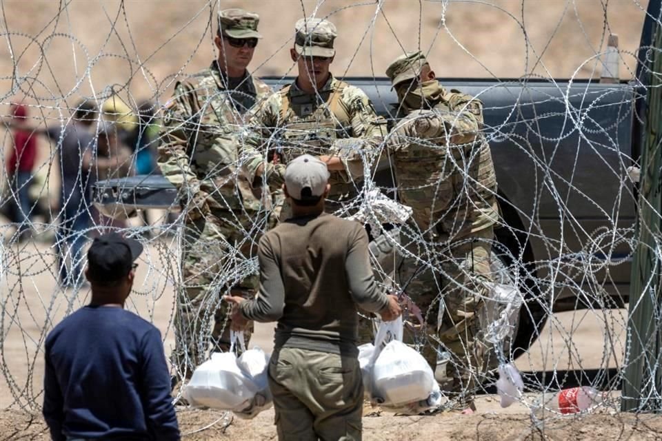 Soldados de la Guardia Nacional de Texas cierran una sección de alambre de púas que rodea un campamento de migrantes improvisado mientras un inmigrante intenta regresar con comida para su familia.