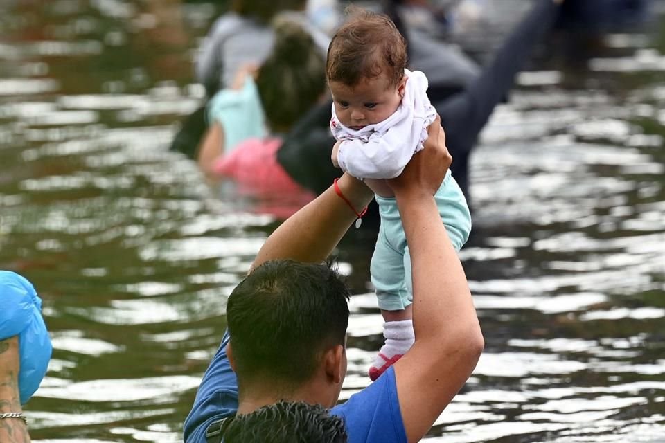 Un migrante con su bebé en brazos trata de cruzar el río para llegar a Estados Unidos.