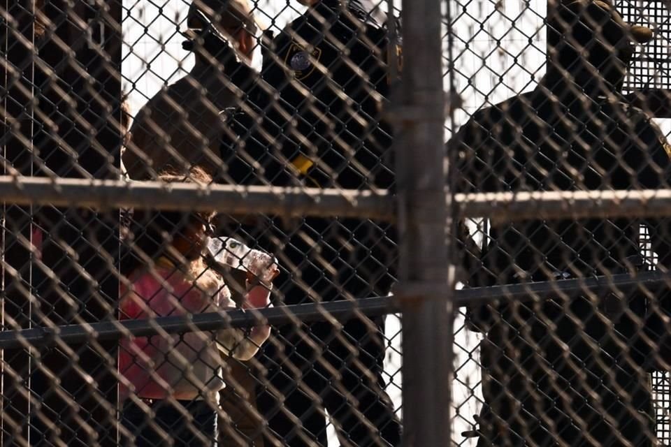 Una niña bebe de una botella de agua mientras los migrantes abordan camionetas de la Patrulla Fronteriza después de esperar a lo largo del muro fronterizo.