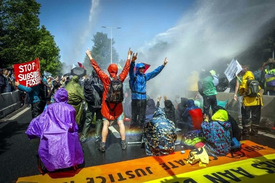 Activistas de Extinction Rebellion (XR) gritan consignas mientras los agentes de policía utilizan un cañón de agua para dispersar su protesta.