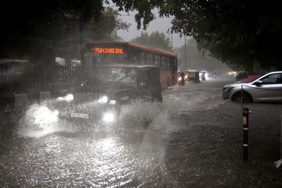 Vehículos se desplazan por una calle inundada de agua durante un fuerte aguacero en Nueva Delhi, India.