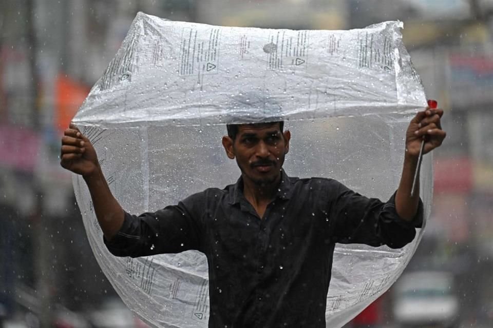 Un hombre se resguarda bajo una bolsa de plástico durante una intensa lluvia en Nueva Delhi.