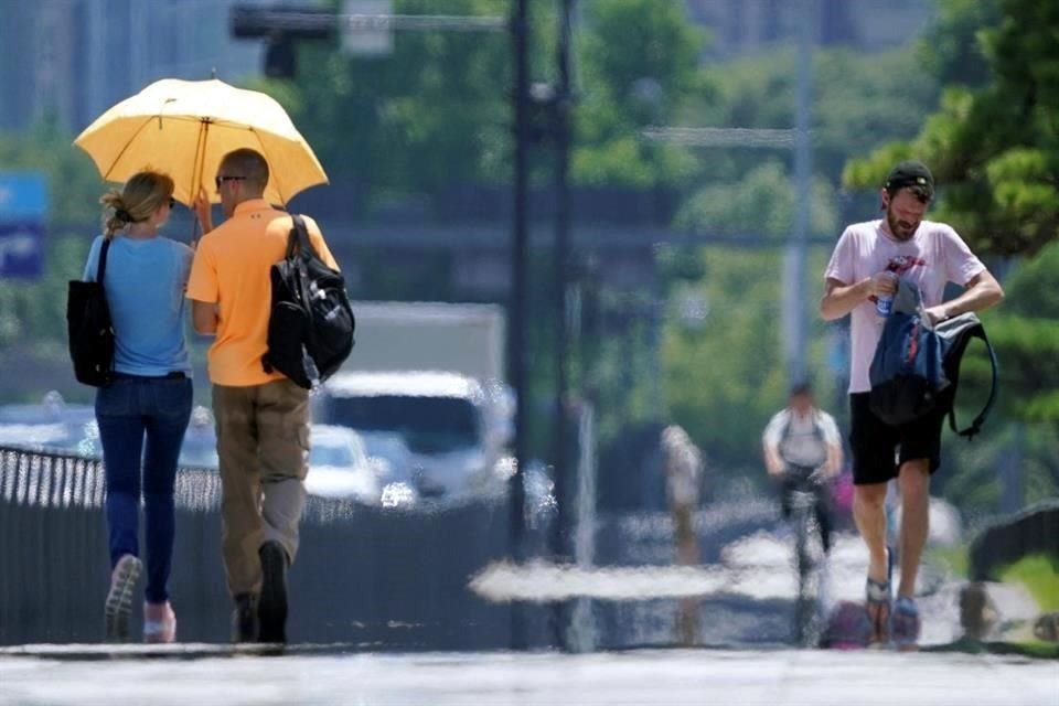 Personas caminan bajo en el intenso calor. 46 millones de personas están bajo aviso de calor excesivo.