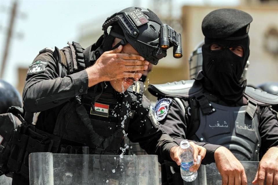 Un miembro de las fuerzas de seguridad iraquíes se enjuaga la cara con agua de una botella para refrescarse durante una ola de calor.