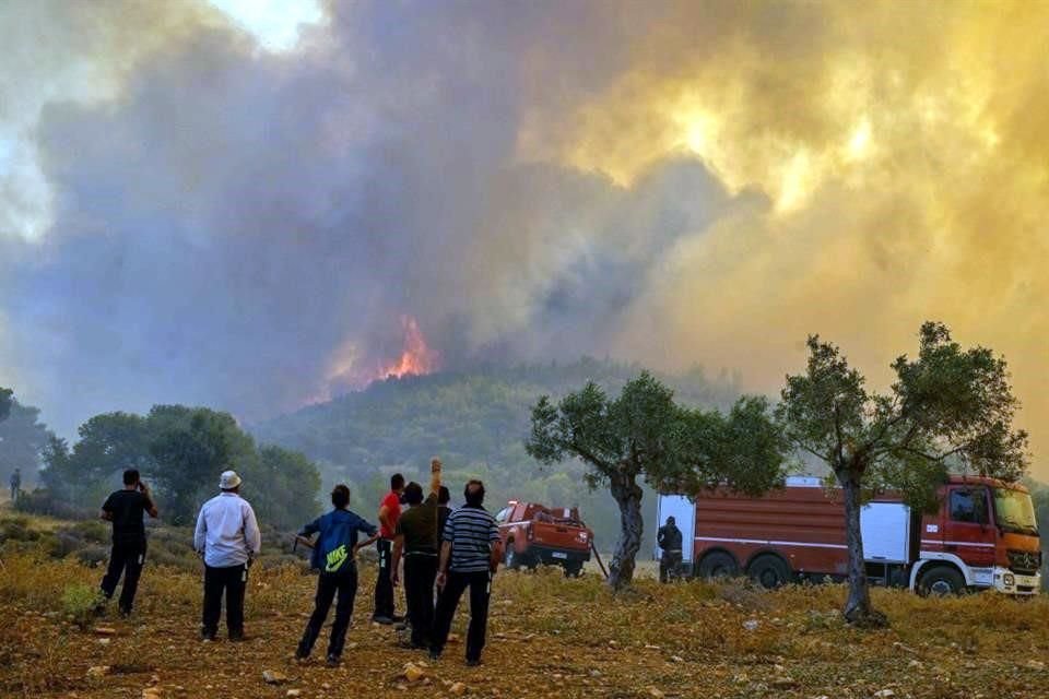 Las personas se paran frente a un incendio forestal en New Peramos, cerca de Atenas.