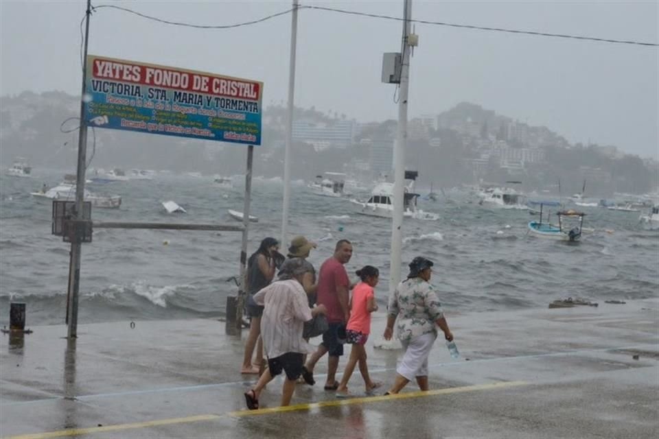 Turistas en Acapulco caminan por la costa que ha sufrido los efectos del huracán 'Hilary'.