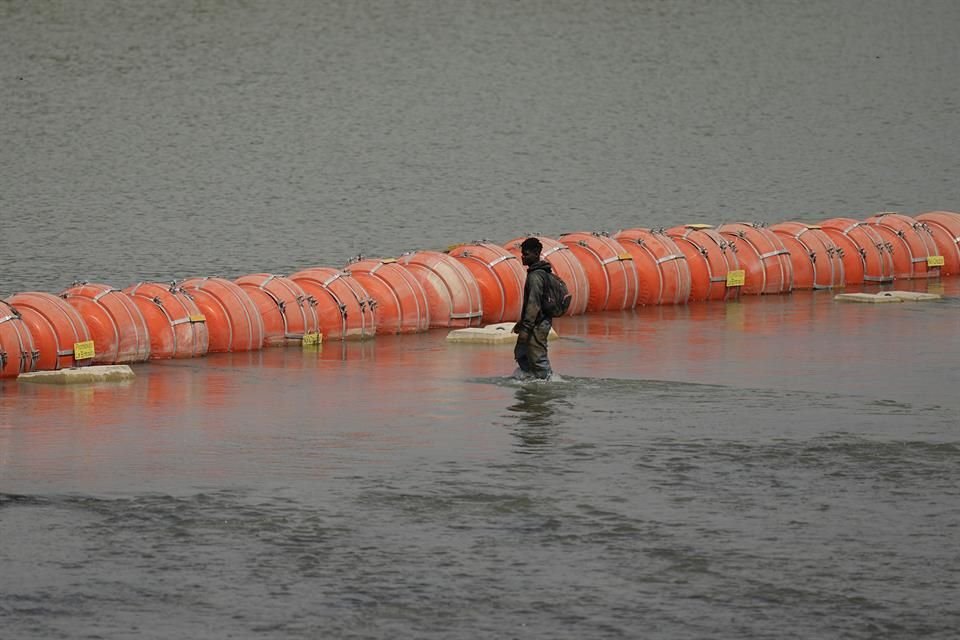 Un migrante colombiano camina a lo largo de la barrera de boyas instalada en el Río Bravo.