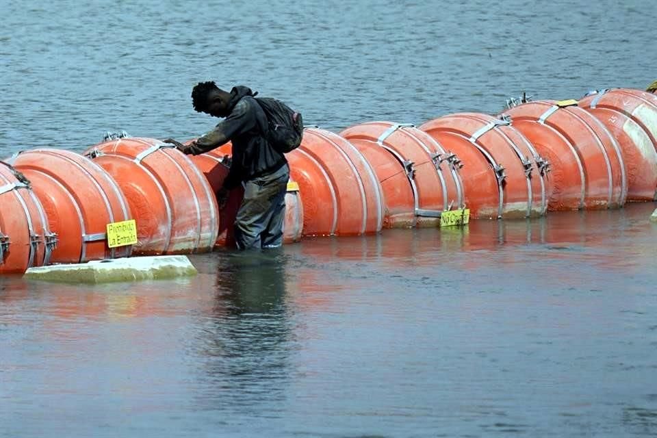 Un migrante reposa en una barrera de boyas flotantes mientras busca cruzar el Río Bravo para llegar a Estados Unidos.