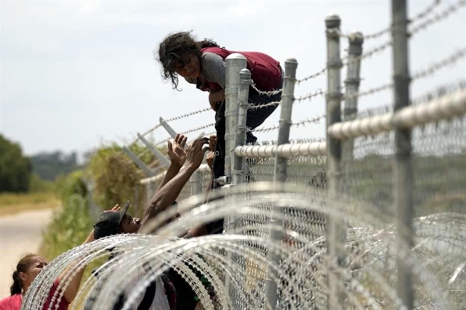 Migrantes que cruzaron el Río Grande de México a Estados Unidos escalan una cerca con alambre de púas.