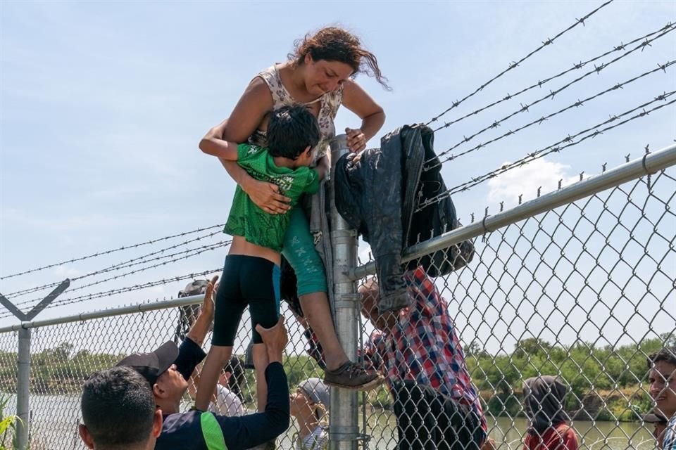 Una mujer ayuda a su hijo a cruzar la frontera entre México y Estados Unidos.