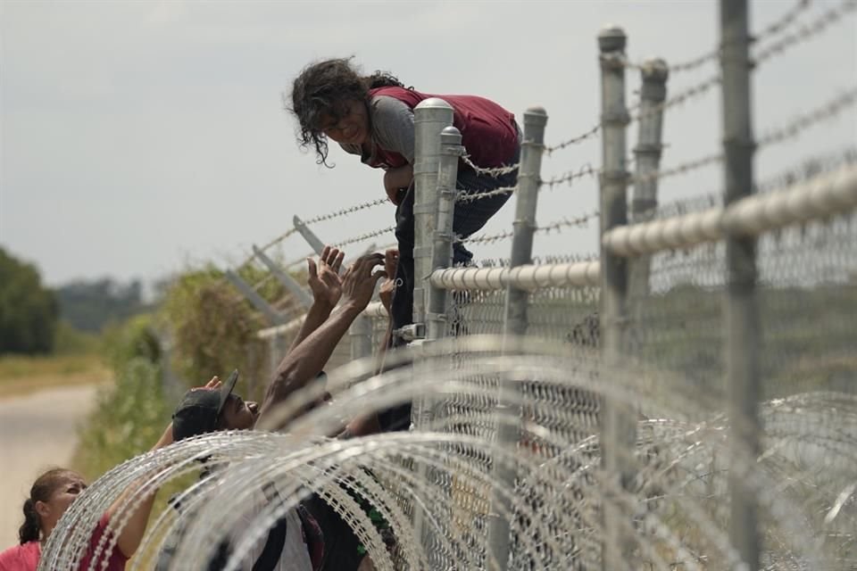 Migrantes que cruzaron el río Grande escalan una cerca con alambre de púas en Eagle Pass.