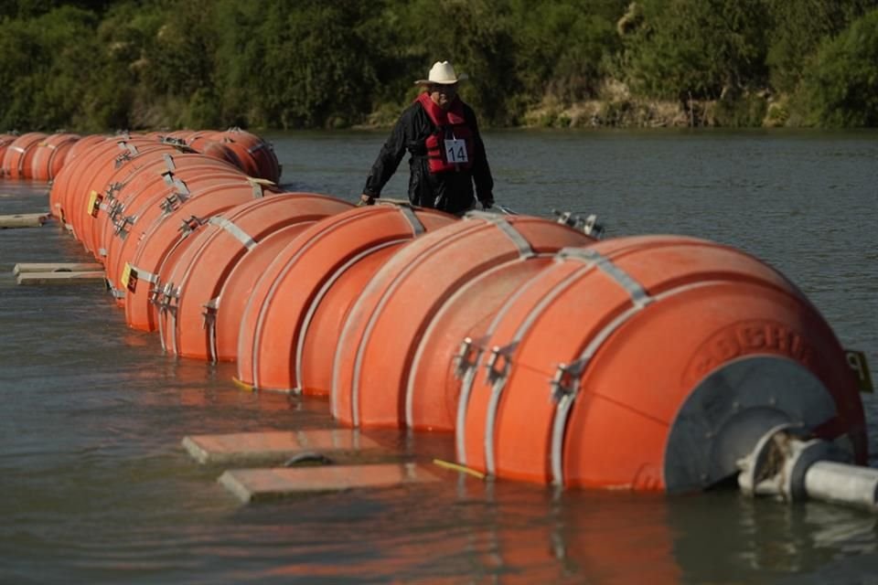 Un hombre camina cerca de una barrera de boyas colocada en el río Bravo, en la frontera entre México y Estados Unidos.