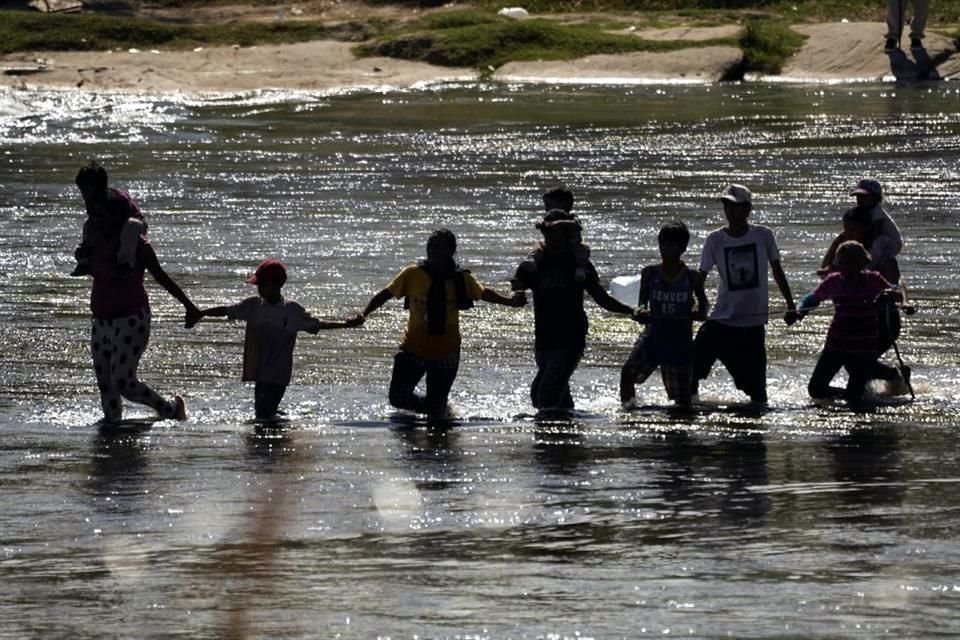 Los migrantes se dan la mano mientras cruzan el Río Bravo desde México hacia EU.