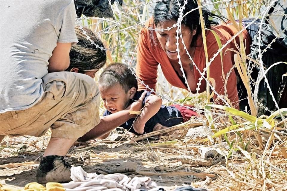 Desafiando el alambre de púas que el Gobernador de Texas, Greg Abbott, ordenó instalar en las orillas del Río Bravo, migrantes pasan a un bebé bajo la cerca para cruzar a Eagle Pass.